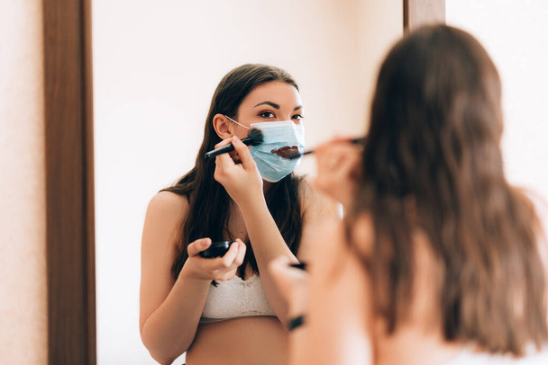 Young beautiful girl makes a make-up in medical mask - Valokuva, kuva