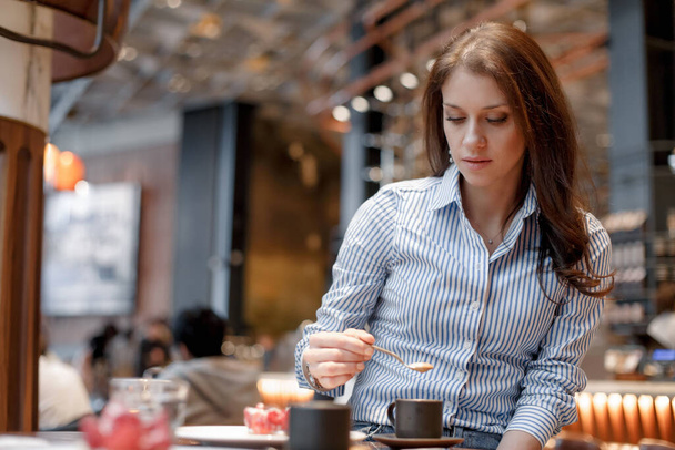 Young beautiful girl in a blue shirt in a beautiful fashionable cafe - Фото, изображение