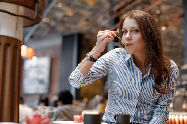 Young beautiful girl in a blue shirt in a beautiful fashionable cafe. Girl eat with a spoon - Foto, Bild