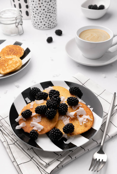 Pannenkoeken met bramen en kokoschips op witte tafel. Zelfgemaakt glutenvrij ontbijt. Kleine crêpes gemaakt van kokosmeel - Foto, afbeelding