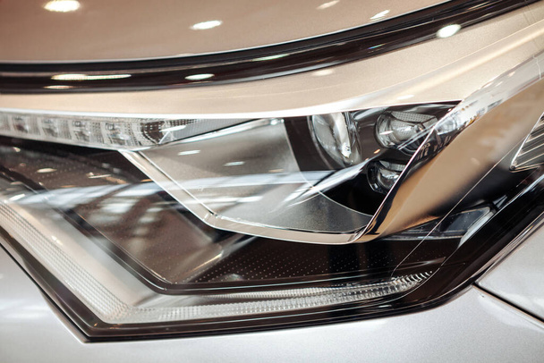 Closeup of a car headlight. Headlight of an expensive new car at a car dealership. - Фото, изображение