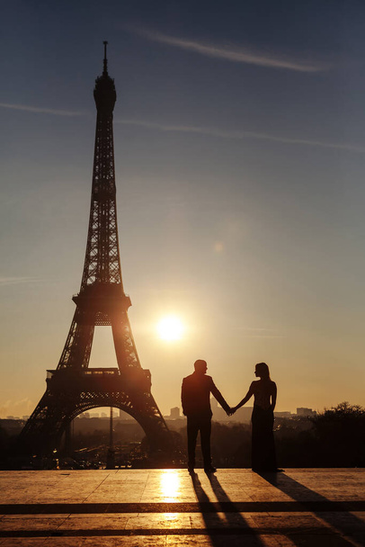 Eyfel Kulesi 'nin arka planında yeni evlilerin silueti var. Çift el ele tutuşuyor ve birbirlerine bakıyor. Paris 'te şafak. - Fotoğraf, Görsel