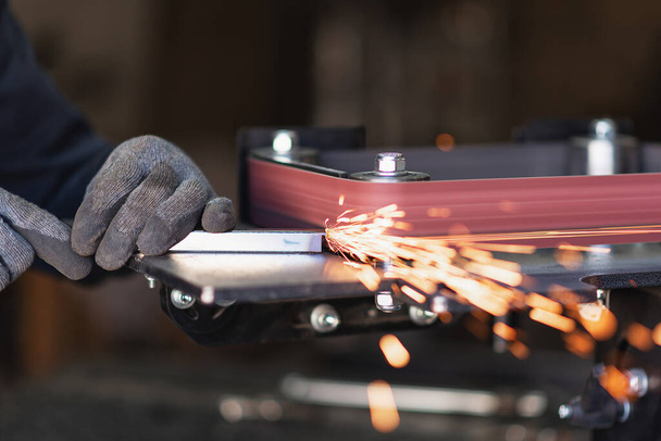 Un ouvrier d'outillage industriel meule un tuyau d'acier carré sur une ponceuse à bande rotative
 - Photo, image