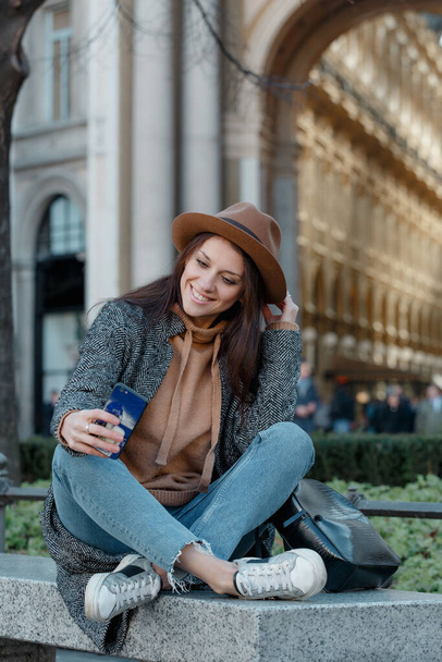 Una joven está sentada en un banco de piedra y sonríe
 - Foto, Imagen