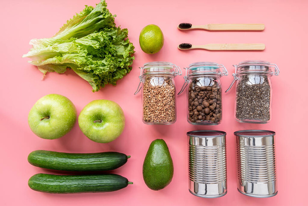 Coronavirus food supplies concept. Vegetables, canned food, wooden toothbrushes layout top view on pink background - Photo, Image