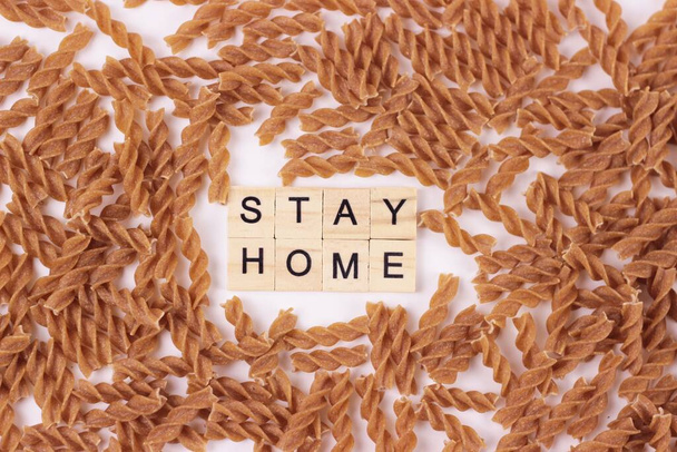 Inscription stay home from wooden letters on macaroni or pasta background.Uncooked pasta on white.The concept of staying at home to avoid spreading the coronavirus.Raw macaroni texture for background - Photo, image