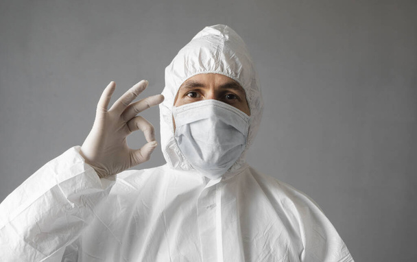 Doctor in white protective suit, medical mask and rubber gloves is showing that everything is fine. Helping a people while coronavirus pandemic threat. Epidemic, pandemic of coronavirus covid 19. - Foto, Imagem