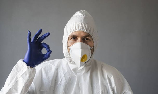 Doctor in white protective suit, medical mask and rubber gloves is showing that everything is fine. Helping a people while coronavirus pandemic threat. Epidemic, pandemic of coronavirus covid 19. - Zdjęcie, obraz