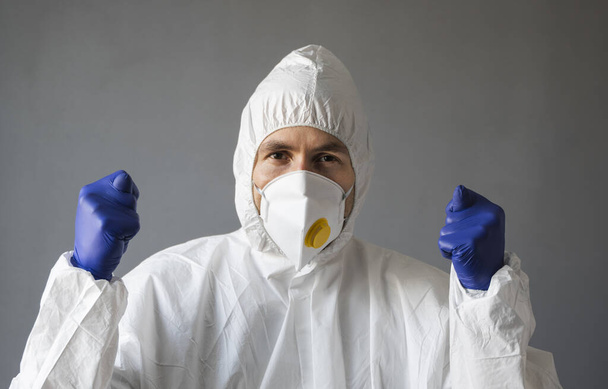Doctor in white protective suit, medical mask and rubber gloves is showing Fig sign to the virus. Helping a people while coronavirus pandemic threat. Epidemic, pandemic of coronavirus covid 19. - Fotoğraf, Görsel