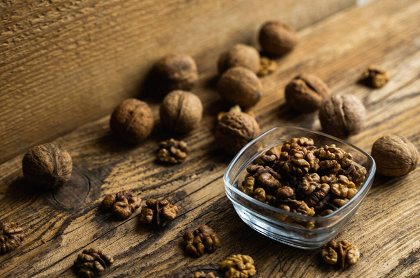 Walnut in a smale plate with scattered shelled nuts and whole nut which standing on a wooden vintage table. Walnuts is a healthy vegetarian protein nutritious food. Walnut on rustic old wood. - Foto, Imagem