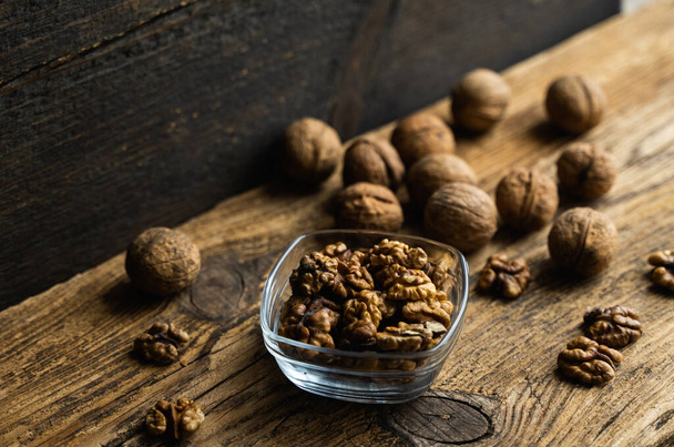 Walnut in a smale plate with scattered shelled nuts and whole nut which standing on a wooden vintage table. Walnuts is a healthy vegetarian protein nutritious food. Walnut on rustic old wood. - Fotoğraf, Görsel