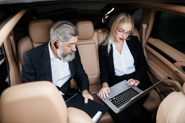 An elderly attractive and bearded man, discussing working moments with his Secretary, in the cabin of an expensive car - Φωτογραφία, εικόνα