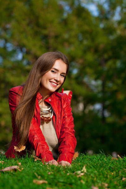 Young beautiful woman in red leather jacket sitting in the autumn park - Фото, зображення