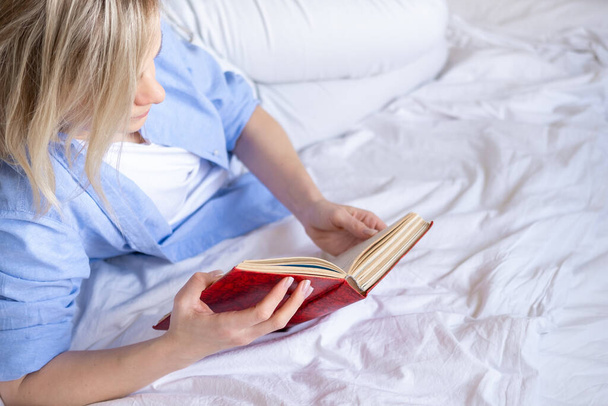 Cropped blonde woman using smartphone sitting on bed. Reading news and online books. Social media, instagram, stay home and quarantine - Foto, afbeelding