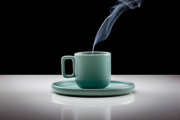 Pastel café de color verde o taza de té con líquido caliente, humo y vapor, fondo negro. Copa de pie sobre una mesa ligeramente reflectante que se desvanece en un fondo negro
 - Foto, Imagen