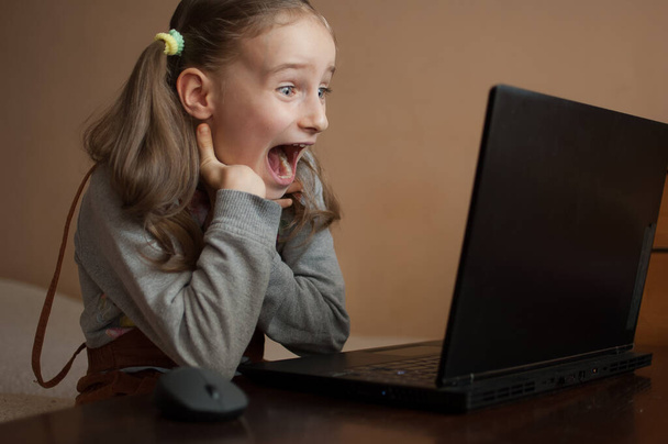 Счастливая взволнованная девочка учится дома со своим учителем, используя видео-чат онлайн на своем черном ноутбуке из-за самоизоляции из-за пандемии Коронавируса Ковид-19. Удаленное образование
 - Фото, изображение