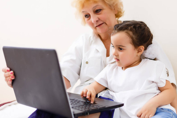 Smart little girl grandchild sit on couch shopping online with excited senior grandmother, teen granddaughter and smiling granny buy on internet browsing laptop relaxing at home together - Photo, Image