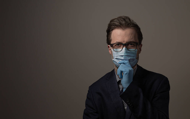 Portrait of thoughtful caucasian businessman while dangerous virus or bacteria epidemic. Man in a suit protected by surgical face mask and disposable gloves. Crisis or recession problem concept. - Fotoğraf, Görsel