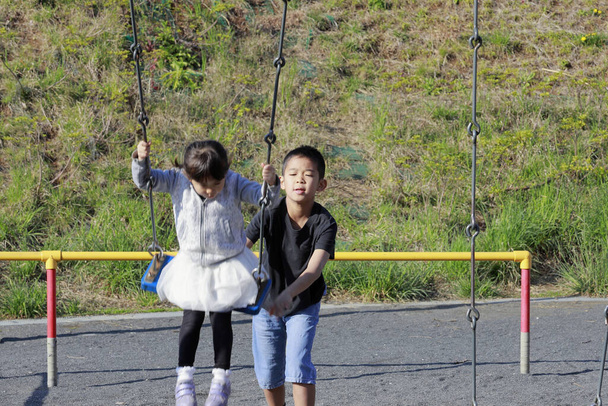 Japanese sister on the swing and brother pushing her back (10 years old boy and 5 years old girl) - Photo, Image