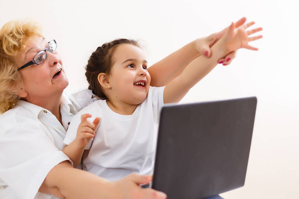 Fiksu pikkutyttö lapsenlapsi istuu sohvalla ostoksia verkossa innoissaan vanhempi isoäiti, teini lapsenlapsi ja hymyilevä mummo ostaa internetissä selailu kannettava tietokone rentouttava kotona yhdessä - Valokuva, kuva