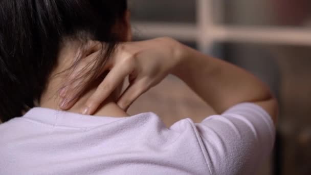 4k Aziatische jonge vrouw masseren haar nek en schouder achteraanzicht close-up, zitten in de woonkamer thuis, zelf massage behandeling, kantoor syndroom, close-up strakke schot. zwart haar model, warm licht - Video
