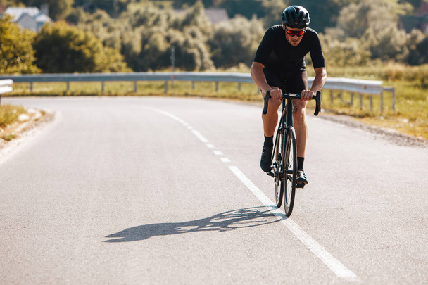 Starker, reifer Mann in Sportbekleidung und Schutzhelm, der schnell unterwegs ist. Radprofi mit Spiegelbrille trainiert regelmäßig, um sich auf Wettkampf vorzubereiten. - Foto, Bild