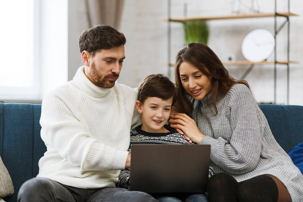 Stay home. Portrait of smiling father, mother and son using laptop for a online meeting, video call, video conference with relatives, home education. Happy family spending time together at home - Foto, Bild