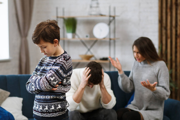 Sad little boy feels upset while his parents fighting at background. Mother and father quarrel. Family conflicts and divorce lead to childrens psychological problem. Childrens mental disorders - 写真・画像