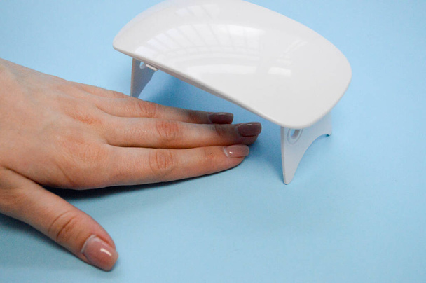 Процес виготовлення красивого манікюру на руках на пальцях за допомогою спеціальної машини і лампи для сушіння лаку в салоні краси нігтів на синьому фоні
 - Фото, зображення