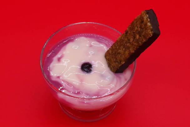 Gesunder Snack mit Apfel-Bananen-Joghurt mit Blaubeeren und Müsliriegel vor rotem Hintergrund. - Foto, Bild