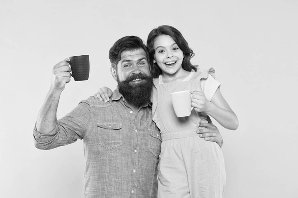 Drink water. Drink fresh juice. Breakfast concept. Good morning. Having coffee together. Healthy lifestyle. Family drinking tea. Bearded man and happy girl holding mugs. Father and daughter hot drink - Фото, изображение