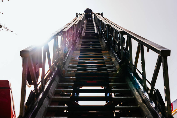 Механическая лестница пожарных, видимая снизу на фоне голубого неба
. - Фото, изображение