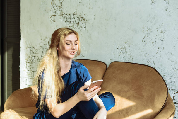 Una giovane donna naviga su internet al telefono e sorride e ride. Sfoglia i social network a casa mentre sei seduto sul divano
 - Foto, immagini