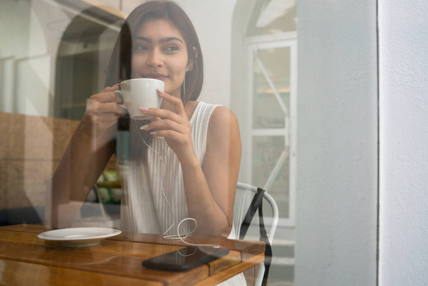 Retrato de una joven latina disfrutando y bebiendo una taza de café en la cafetería. Concepto de estilo de vida. - Foto, imagen