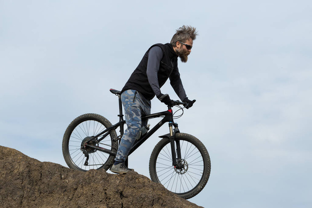 Sports brutal bearded guy on a modern mountain bike. Beautiful view from the mountain. Panoramic view for banner. - Photo, Image