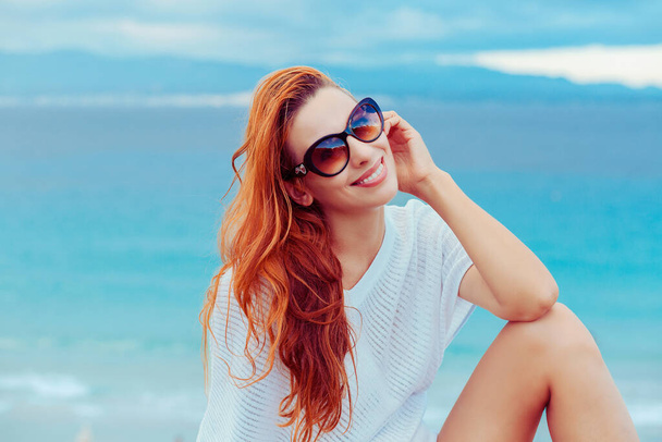 Outdoor fashion closeup portrait summer beach style of young beautiful cute woman fresh face smiling on the sea beach of Sardinian island having fun on vacation in white shirt and sunglasses - Photo, image