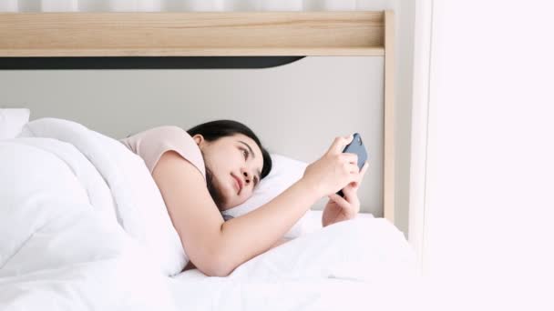 Joven feliz asiático mujer usando su smartphone en la cama en la mañana
. - Imágenes, Vídeo