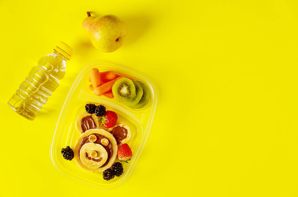 Kids food in lunch boxes with water and pear on yellow background. - Photo, Image