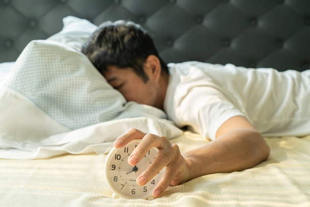 Asiatique homme se réveiller le matin et la main atteignant réveil
 - Photo, image
