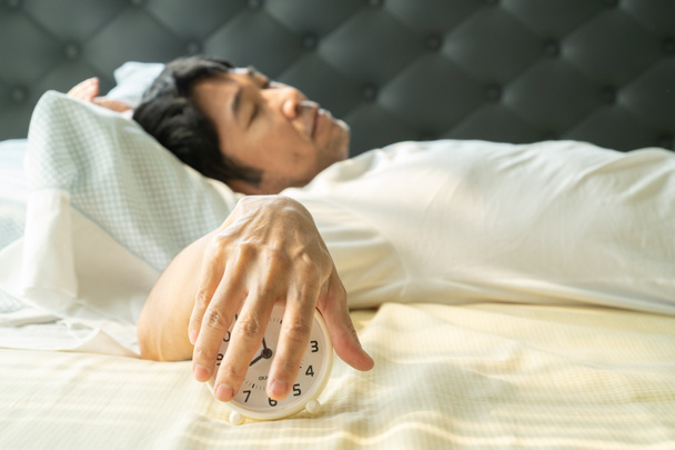 Asiatique homme se réveiller le matin et la main atteignant réveil
 - Photo, image