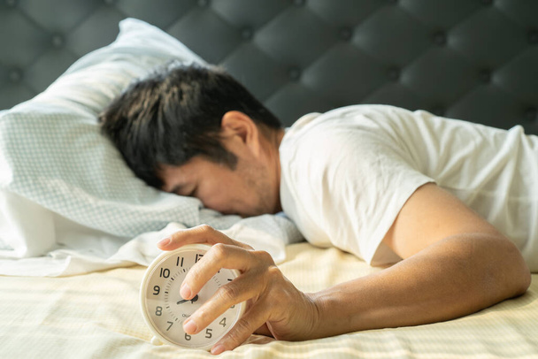 Азиатский мужчина просыпается утром и руки достижения будильник
 - Фото, изображение