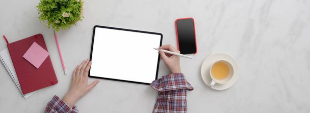 Top view női szabadúszó dolgozik üres képernyő tabletta, okostelefon, kellékek és teáscsésze márvány asztalon   - Fotó, kép