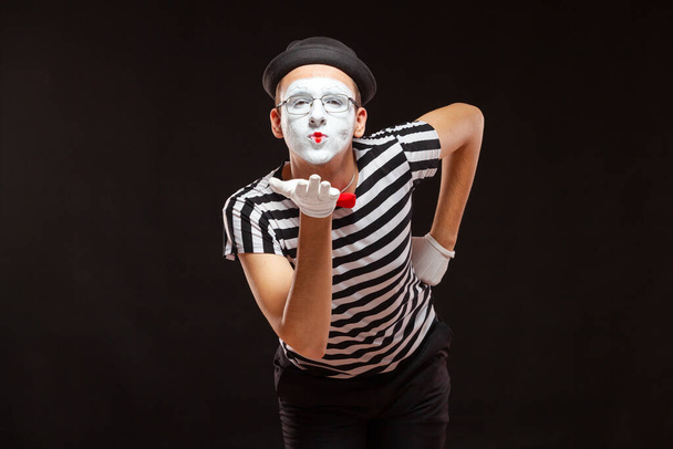 Portrait of male mime artist performing, isolated on black background. Man leaned over to blow a kiss - Fotó, kép