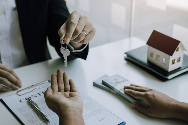 Рука агента по недвижимости передает ключ новым домовладельцам в офисе с концепцией дома покупателя. - Фото, изображение