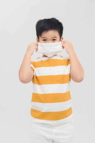 Ένα μικρό αγόρι κρατάει μια ιατρική μάσκα. Το μωρό φοράει μάσκες προσώπου covid-19. - Φωτογραφία, εικόνα
