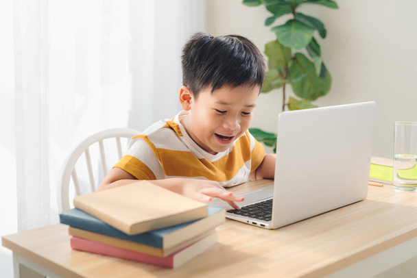 Schooljongen spelen online spel op laptop thuis zittafel, pretienervrije tijd - Foto, afbeelding