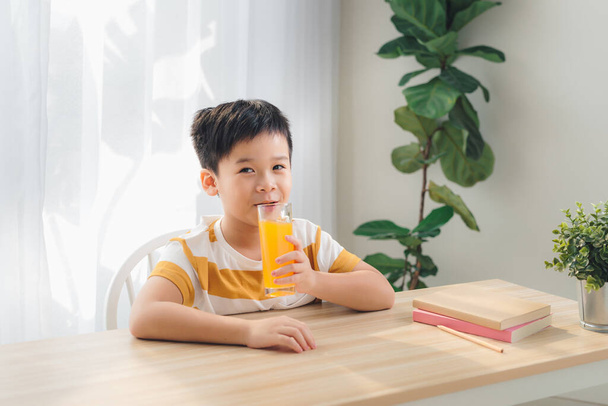 happy child drinking orange juice, sitting at a table and smiling  - Foto, imagen