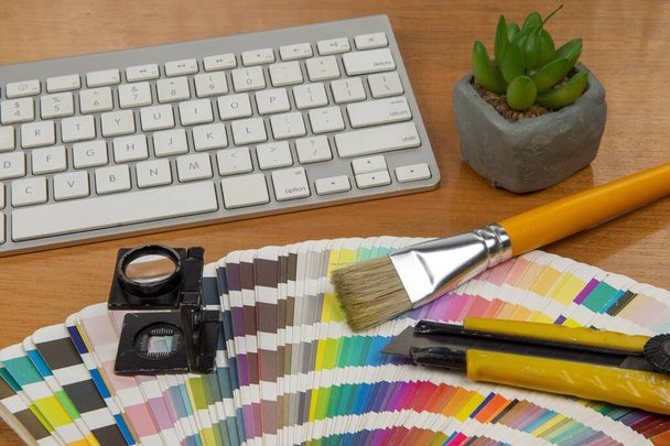 kleurschaal met stylus en vergrootglas erop en een notebook en toetsenbord om een element van de creatieve kantooromgeving te vormen - Foto, afbeelding