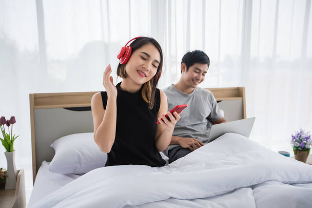The couple put on their headphones and listened to music on their mobile phones on the couch and they were dancing happy in the house for social distance and self responsibility concept - Foto, imagen