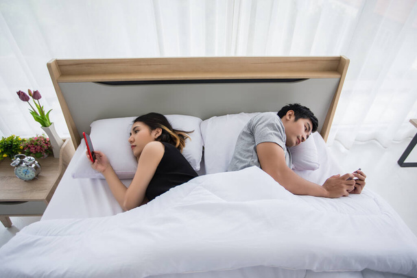 Asiatique couple amoureux couché sur leur jouer téléphones mobiles sur le lit à la maison
 - Photo, image